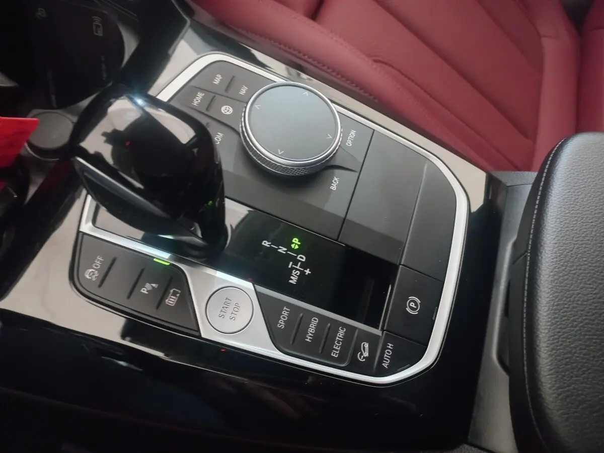 Vue rapprochée de la console centrale noire avec levier de vitesses et molette de sélection, sièges en cuir rouge visibles.