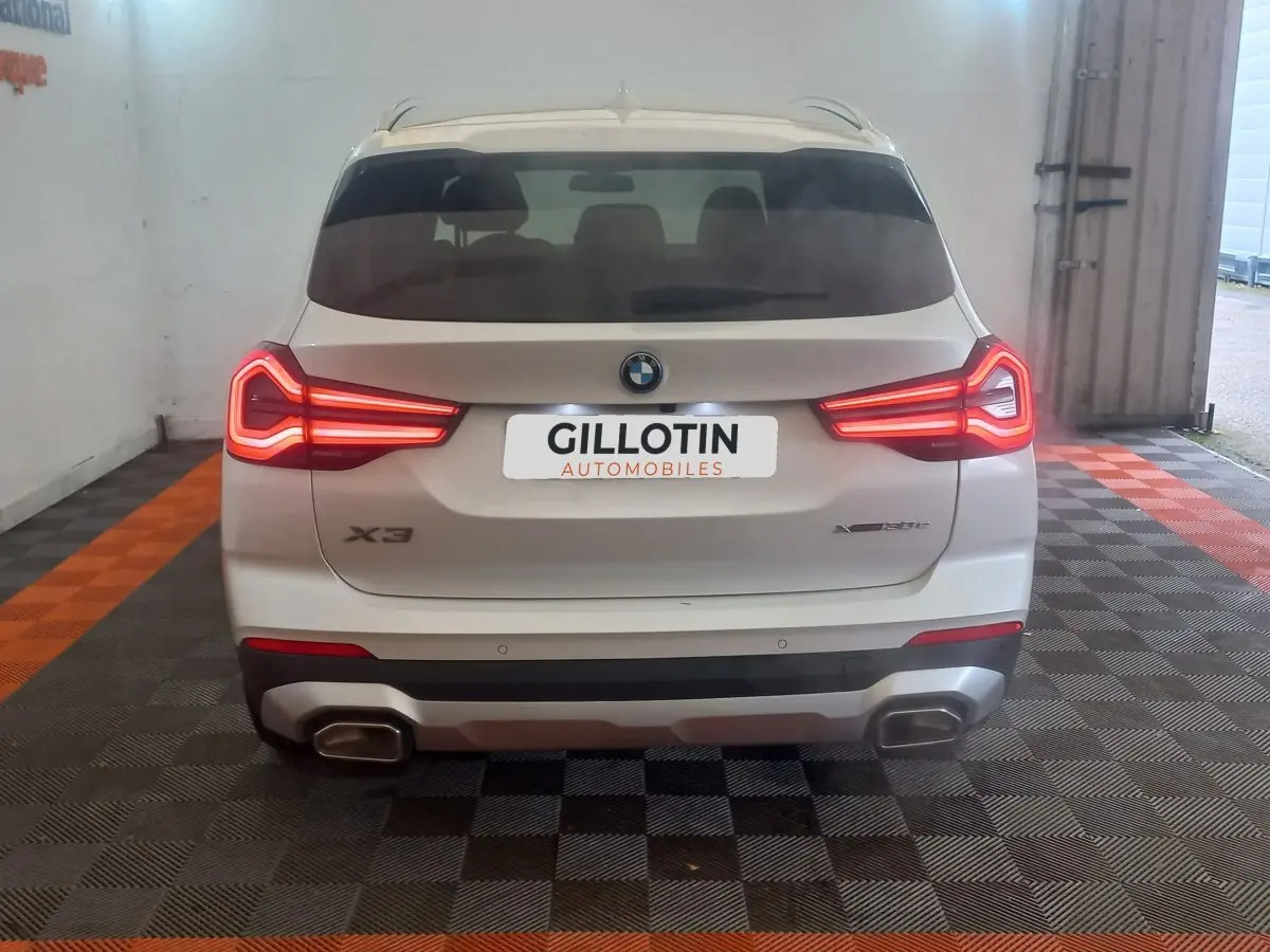 Vue arrière d'un BMW X3 xDrive30e blanc avec feux LED allumés et double sortie d'échappement rectangulaire.