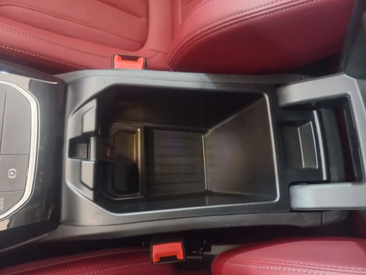 Gros plan sur le rangement central noir entre les sièges rouges du BMW X3 xDrive30e 2022.