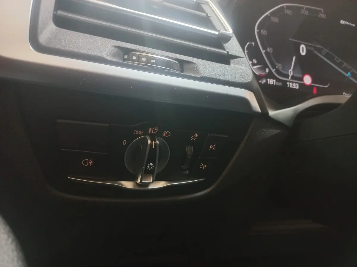 Gros plan sur le commodo des phares et tableau de bord numérique côté gauche d'une BMW X3 blanche hybride rechargeable.