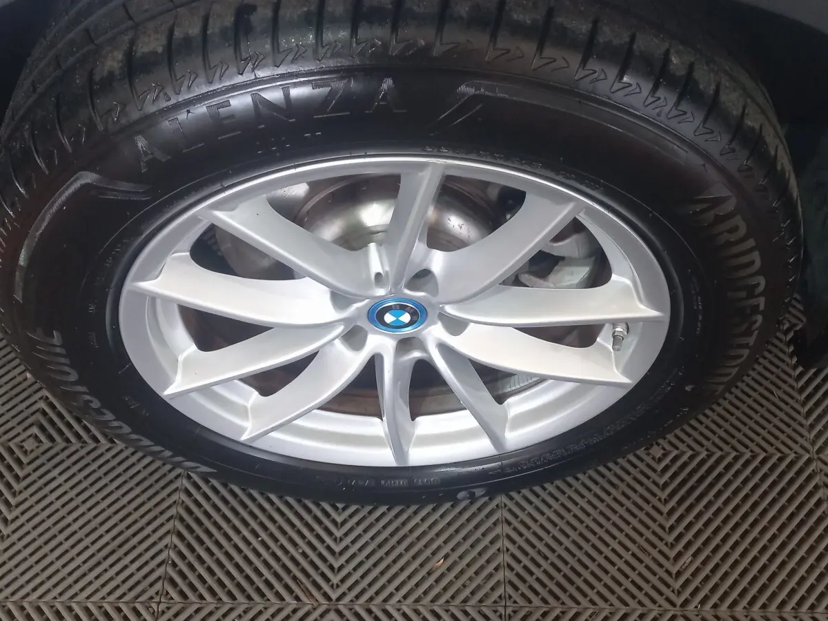 Gros plan sur la jante argentée et le pneu Bridgestone d’un BMW X3 blanc, mettant en valeur le logo central bleu.