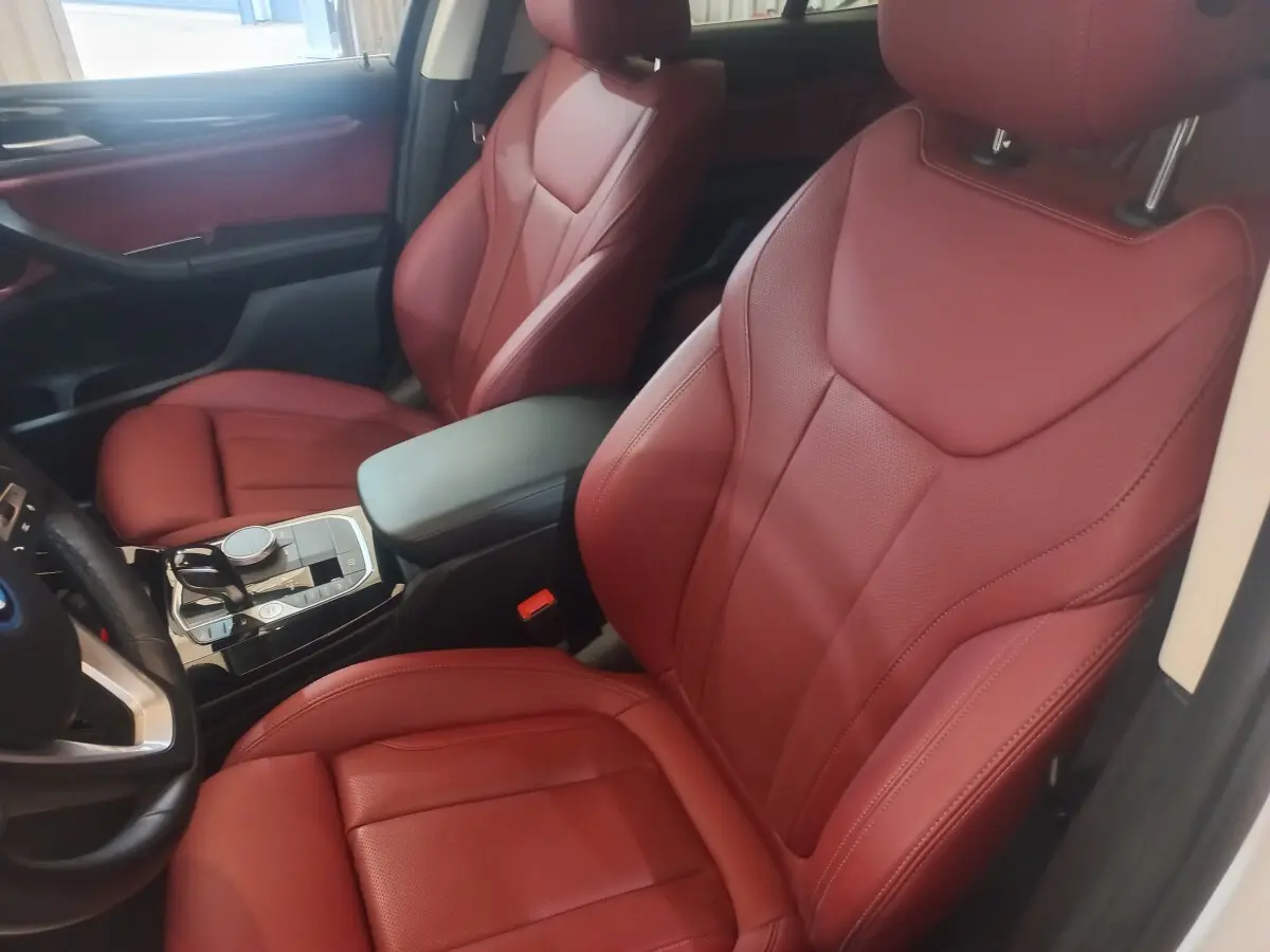 Vue intérieure côté conducteur du BMW X3 blanc 2022, sièges avant en cuir rouge et console centrale moderne.