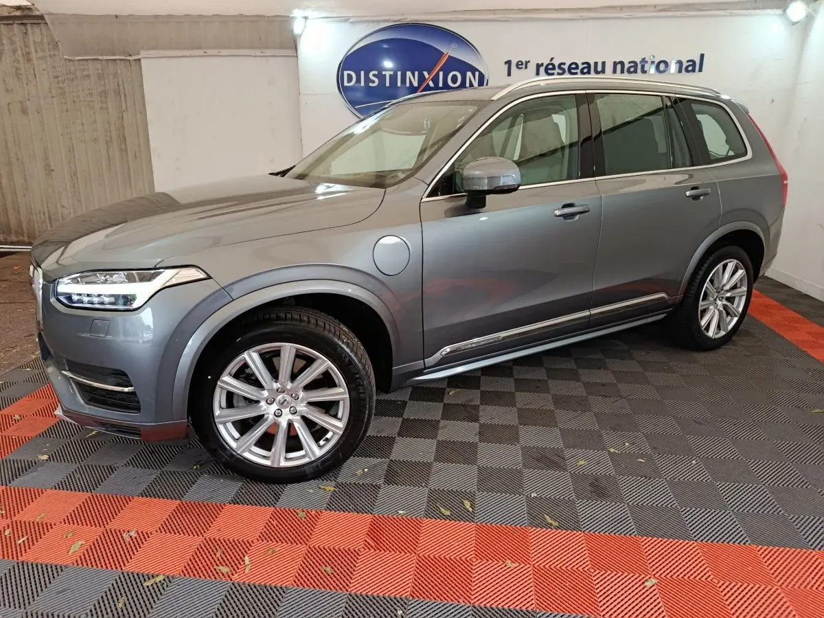 Vue de profil côté gauche d'un Volvo XC90 gris clair hybride rechargeable stationné en intérieur avec jantes alliage visibles.