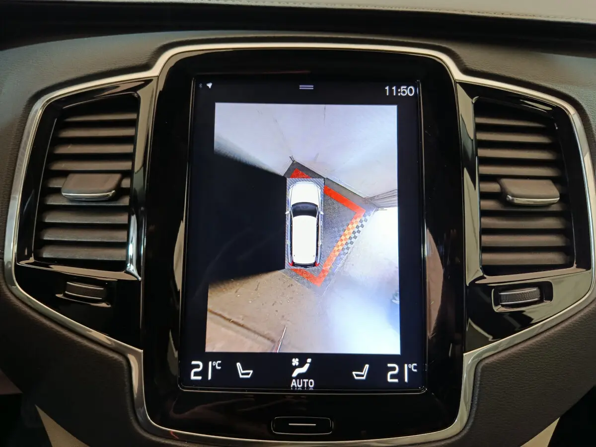 Écran tactile central montrant vue aérienne du Volvo XC90 gris clair en stationnement, tableau de bord noir brillant.