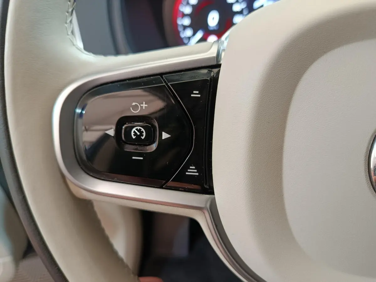 Gros plan sur les commandes de régulateur de vitesse au volant cuir beige du Volvo XC90 T8 hybride rechargeable.