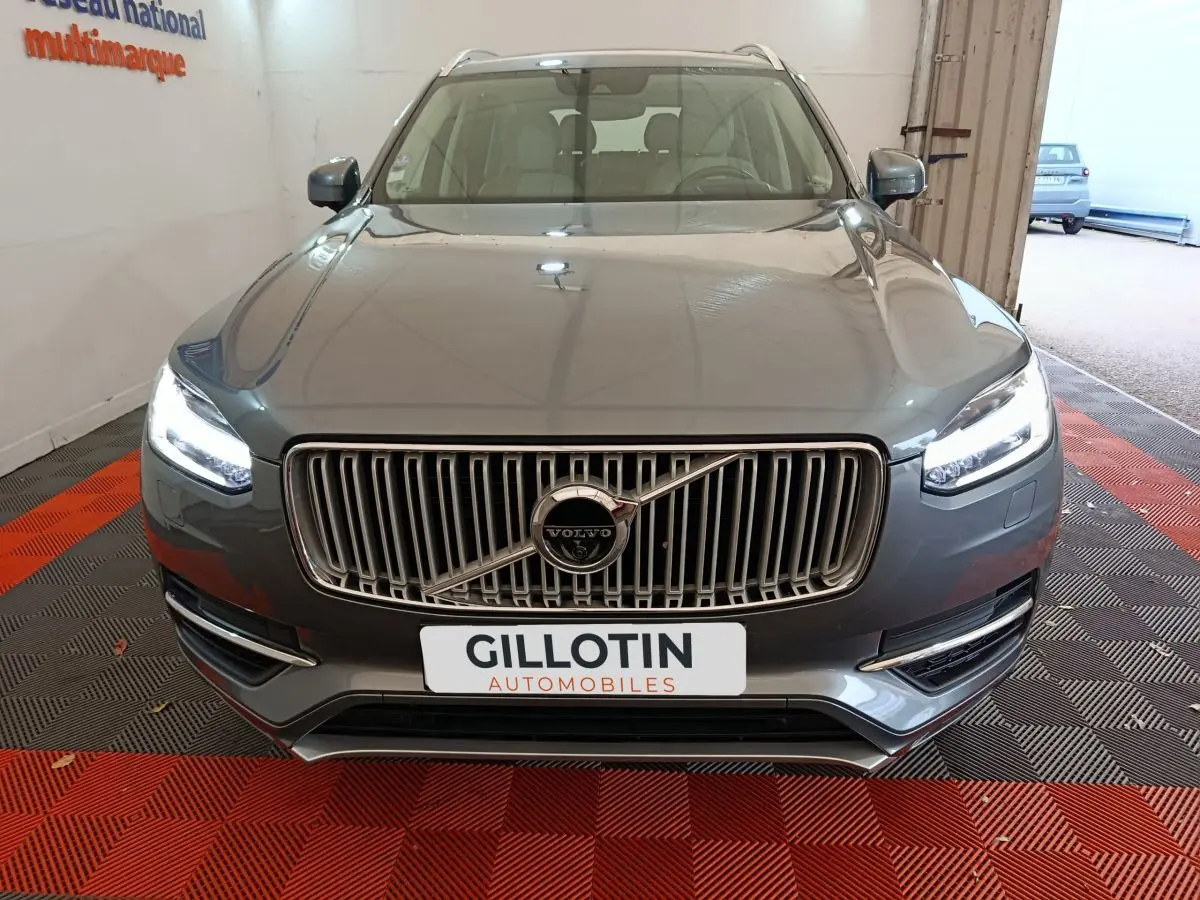 Vue frontale d'un Volvo XC90 gris clair avec calandre verticale chromée et phares LED allumés.