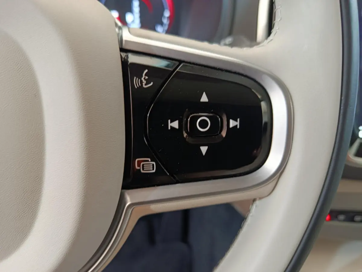 Gros plan sur les commandes noires du volant cuir beige du Volvo XC90 T8 hybride rechargeable, côté gauche.