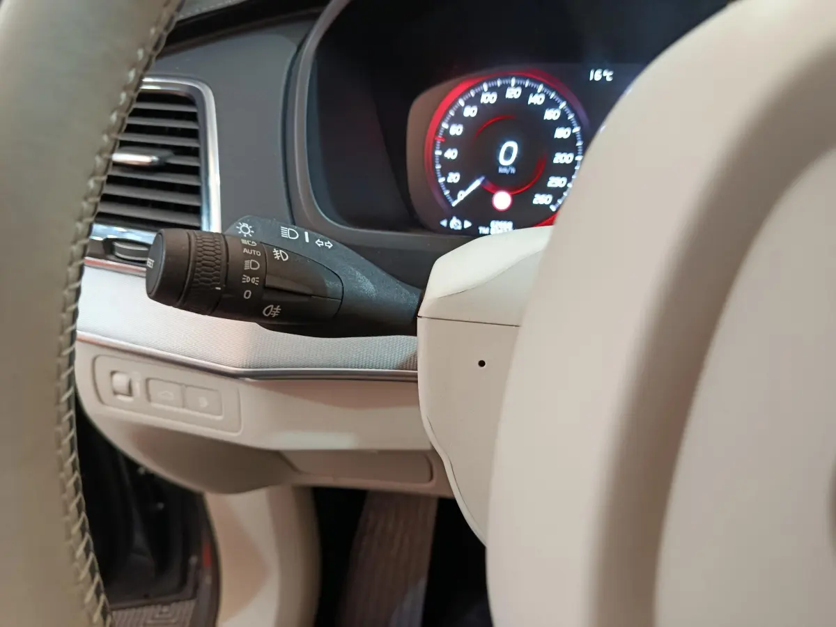 Détail du commodo d'éclairage et tableau de bord numérique affichant 0 km/h dans un Volvo XC90 T8 gris clair.