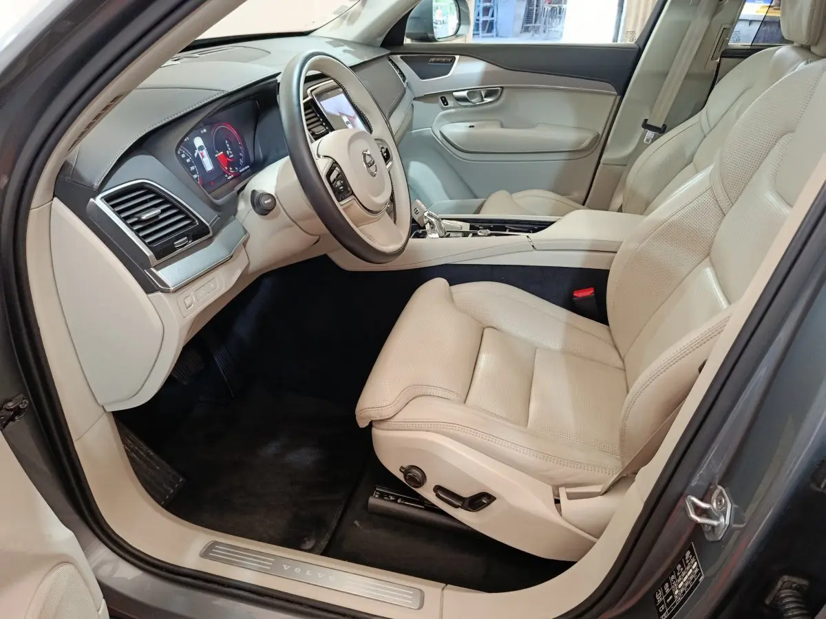 Intérieur côté conducteur du Volvo XC90 gris clair, sièges cuir beige et tableau de bord moderne avec écran digital.