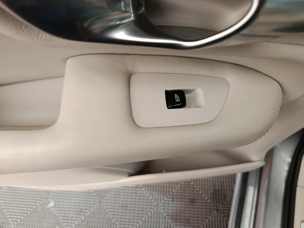 Bouton de commande de lève-vitre sur la porte intérieure beige du Volvo XC90 gris clair, vue côté conducteur.