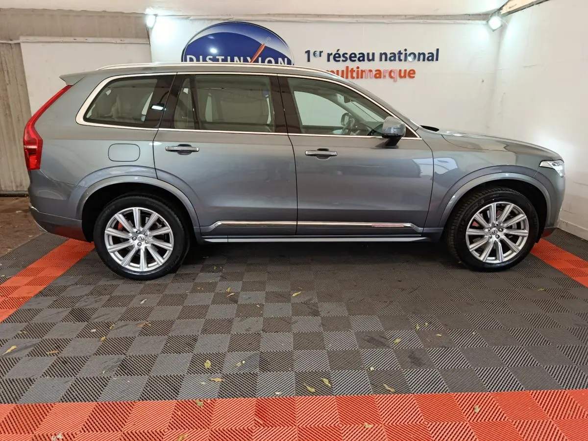 Vue de profil côté gauche d'un Volvo XC90 gris clair, SUV hybride rechargeable avec jantes alliage et toit ouvrant.