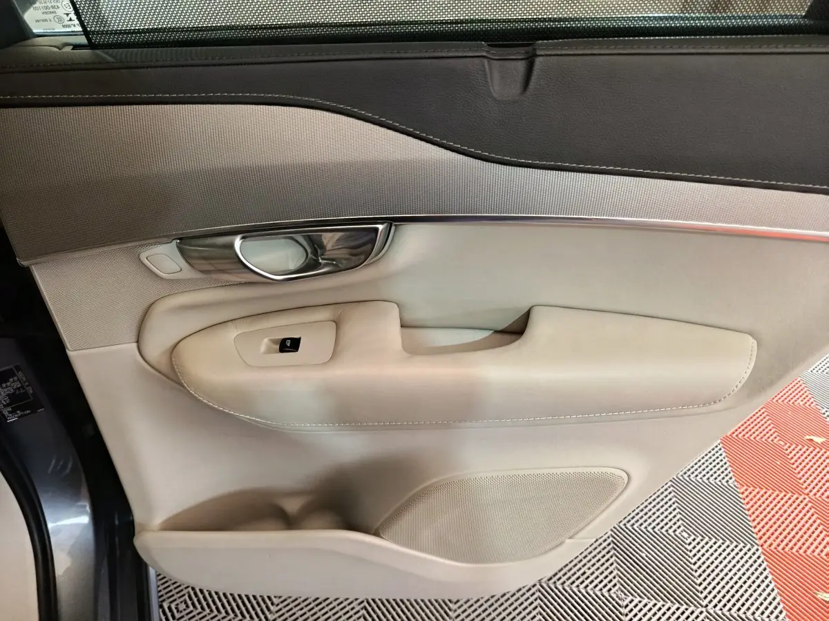 Gros plan sur la porte côté gauche beige et gris clair du Volvo XC90 T8 hybride rechargeable, avec poignée chrome et bouton vitre.