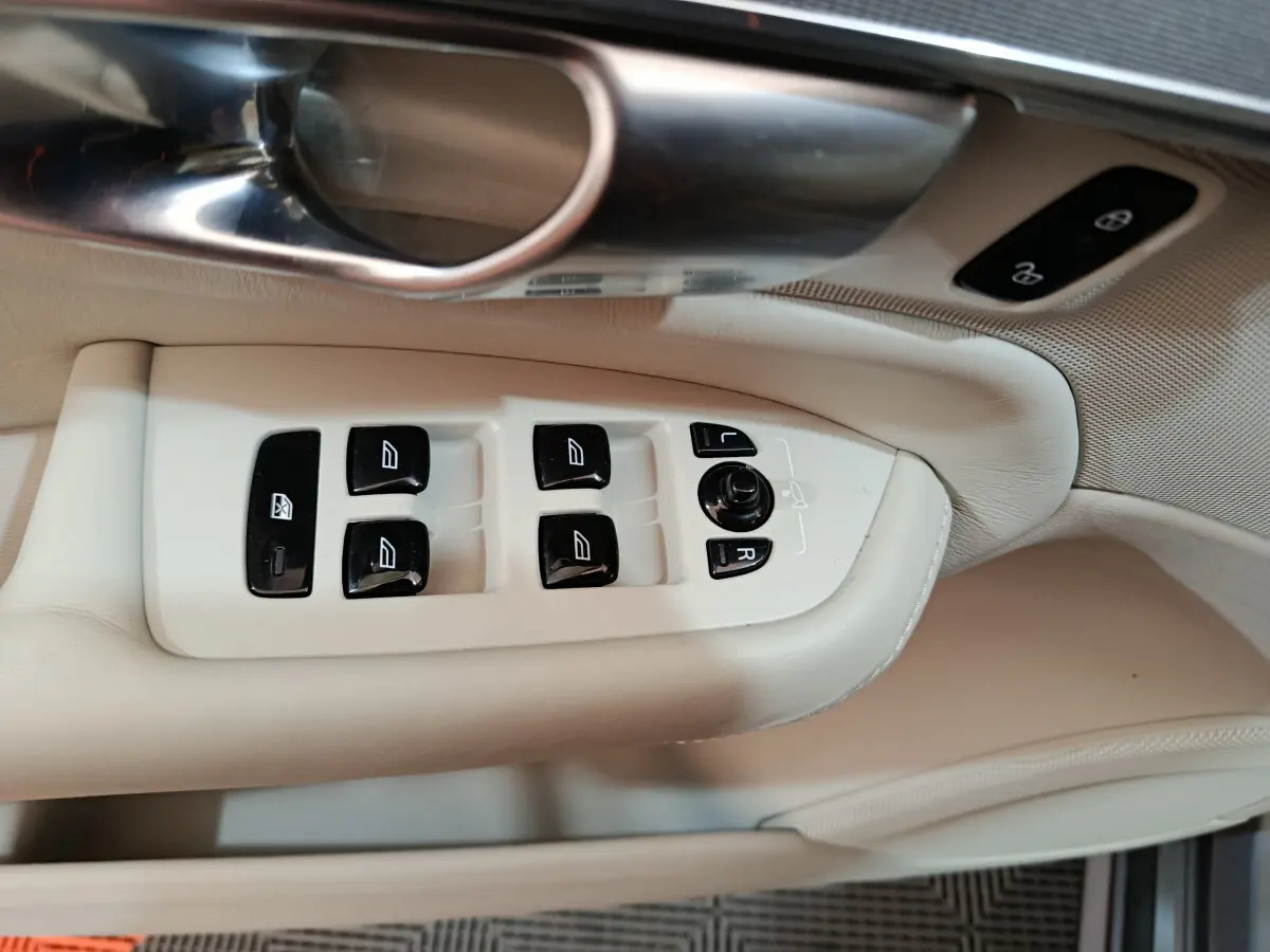 Gros plan sur les commandes de lève-vitres et rétroviseurs côté conducteur en cuir beige clair du Volvo XC90 T8 hybride.