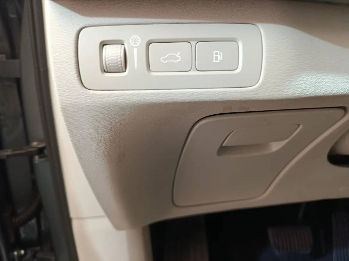 Détail intérieur montrant les commandes d'ouverture du coffre et du réservoir sur la planche côté conducteur du Volvo XC90 gris clair.