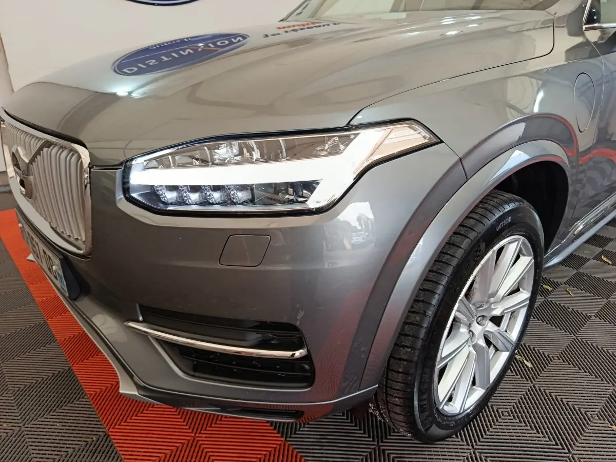 Vue 3/4 avant droit du Volvo XC90 gris clair mettant en valeur son phare LED distinctif et sa calandre verticale chromée.