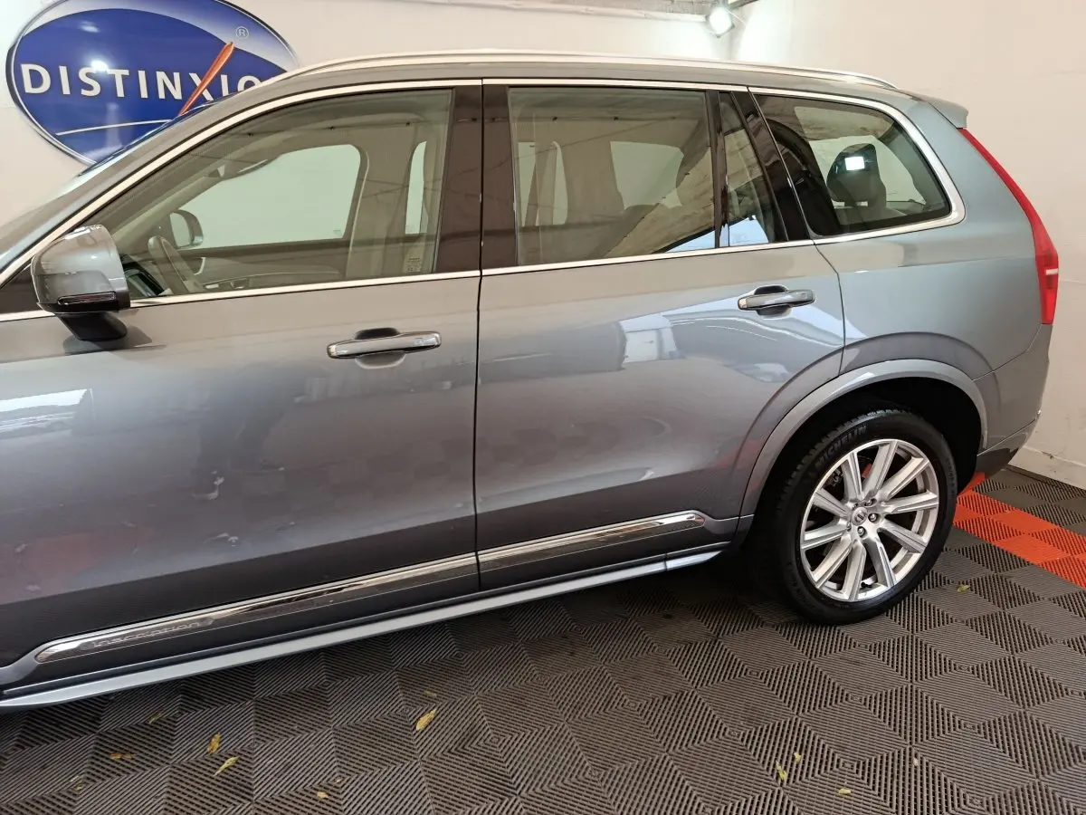 Vue latérale côté gauche d'un Volvo XC90 gris clair avec jantes alliage et vitres teintées.