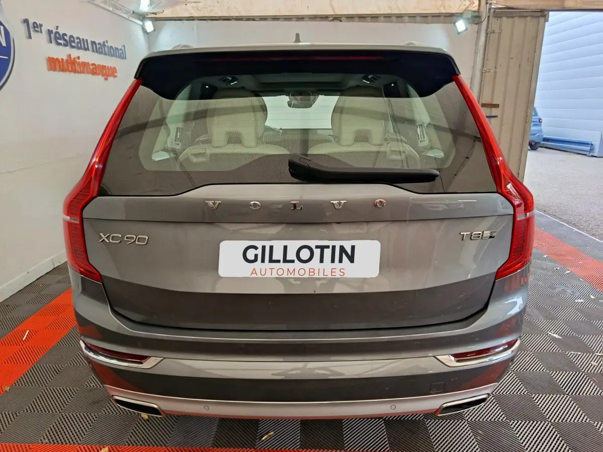 Vue arrière d'un Volvo XC90 T8 gris clair, avec feux arrière verticaux et logo visible sur coffre.