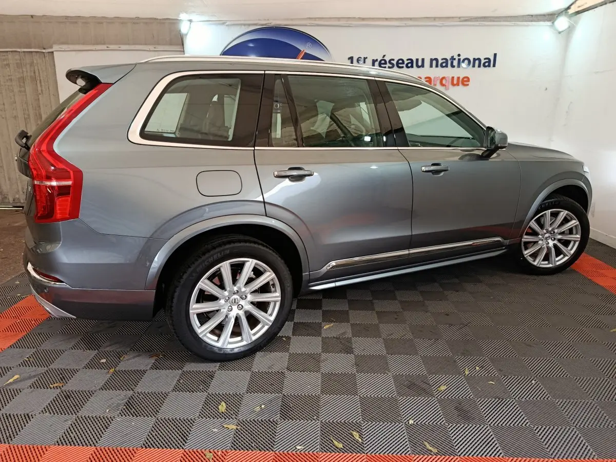 Vue de profil côté gauche d'un Volvo XC90 gris clair, mettant en valeur ses jantes alliage et ses lignes élégantes.