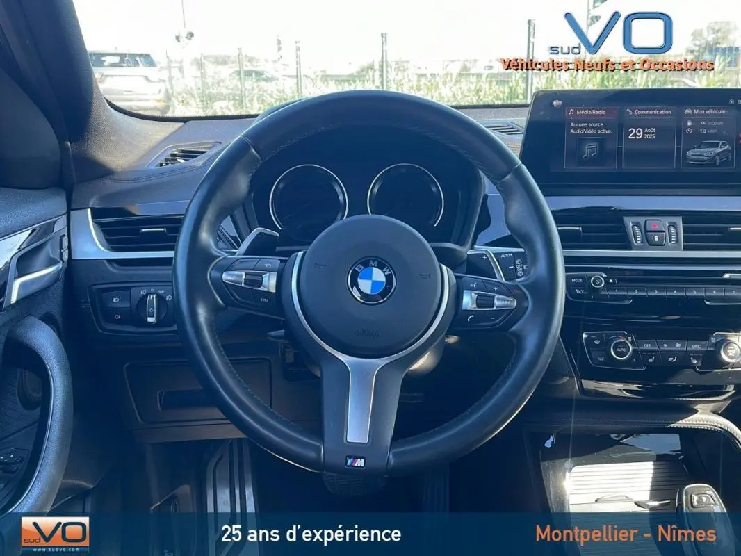 Vue intérieure centrée sur le volant cuir noir du BMW X2 F39 M35i avec tableau de bord et écran multimédia visible.