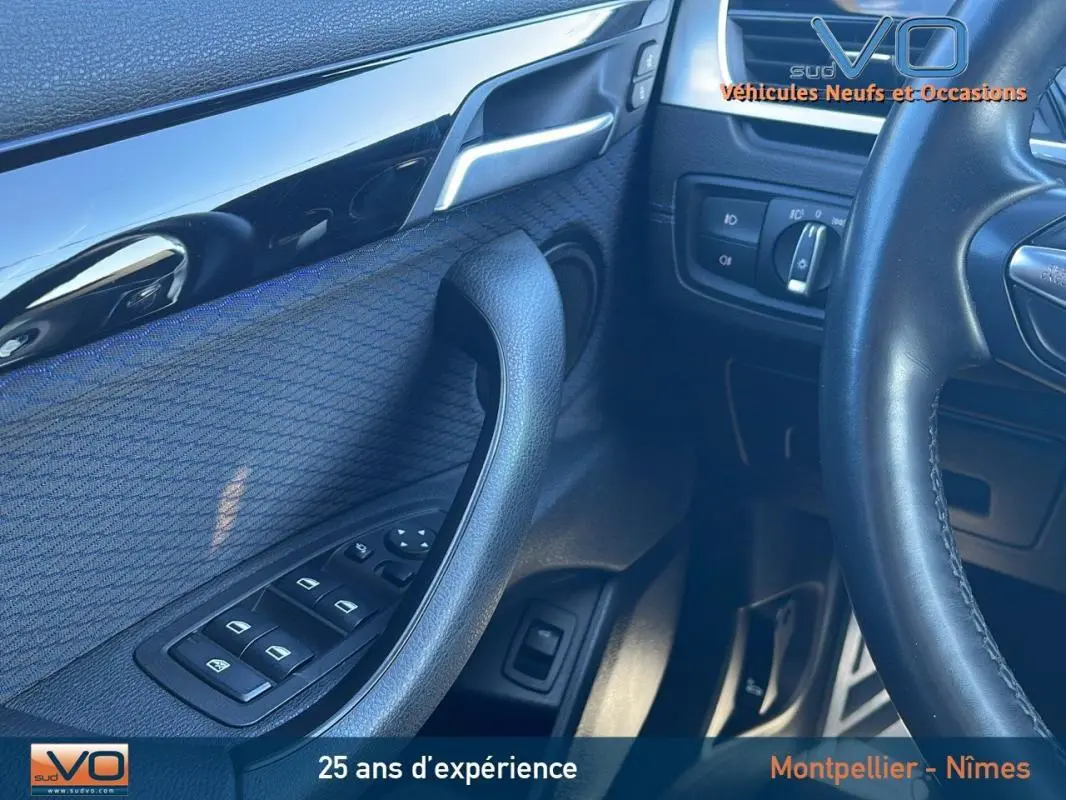 Intérieur côté conducteur du BMW X2 gris, montrant la portière avec commandes des vitres et volant partiel en cuir noir.