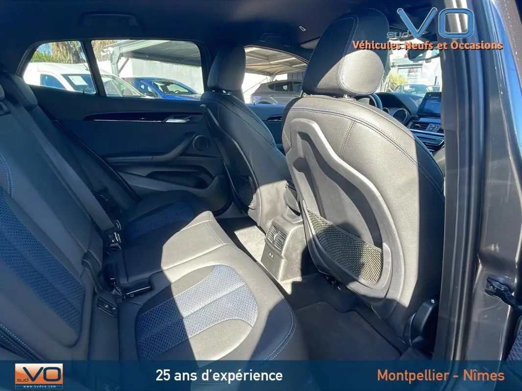 Vue intérieure arrière côté droit du BMW X2 gris, montrant les sièges en cuir et les aérations centrales.