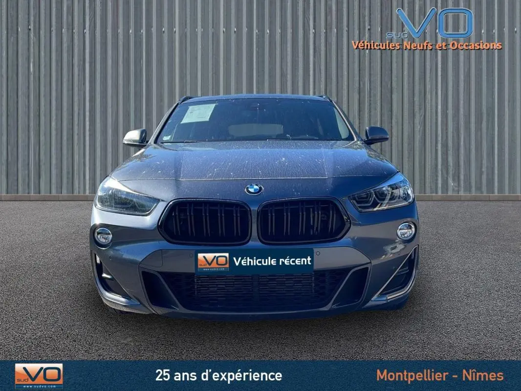 Vue frontale d'un BMW X2 F39 M35i gris 2019 avec calandre noire et phares LED allumés sur fond industriel.