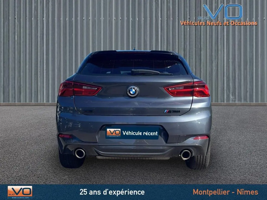 Vue arrière d'un BMW X2 F39 M35i gris avec double sortie d'échappement et feux arrière allumés.