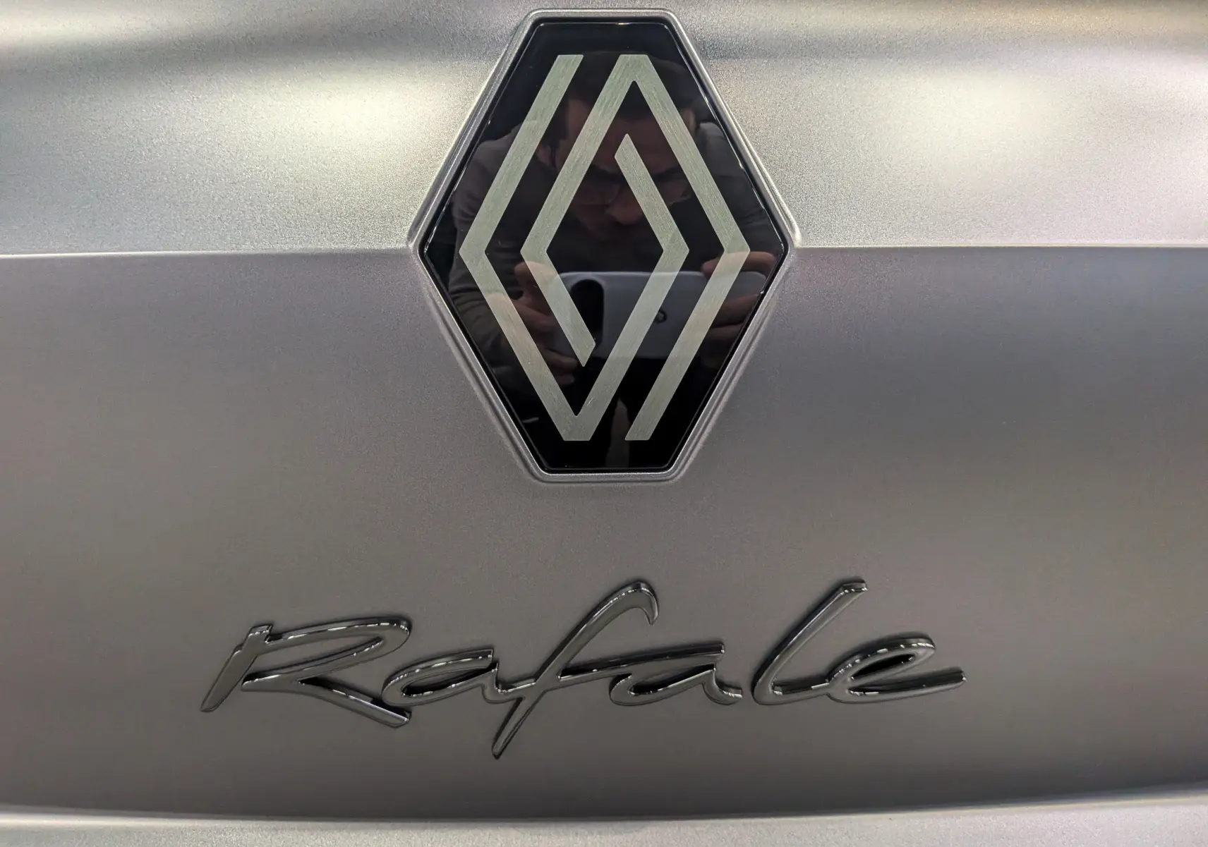 Gros plan sur l'emblème Renault et le logo Rafale en finition Gris Schiste Satin sur la carrosserie.