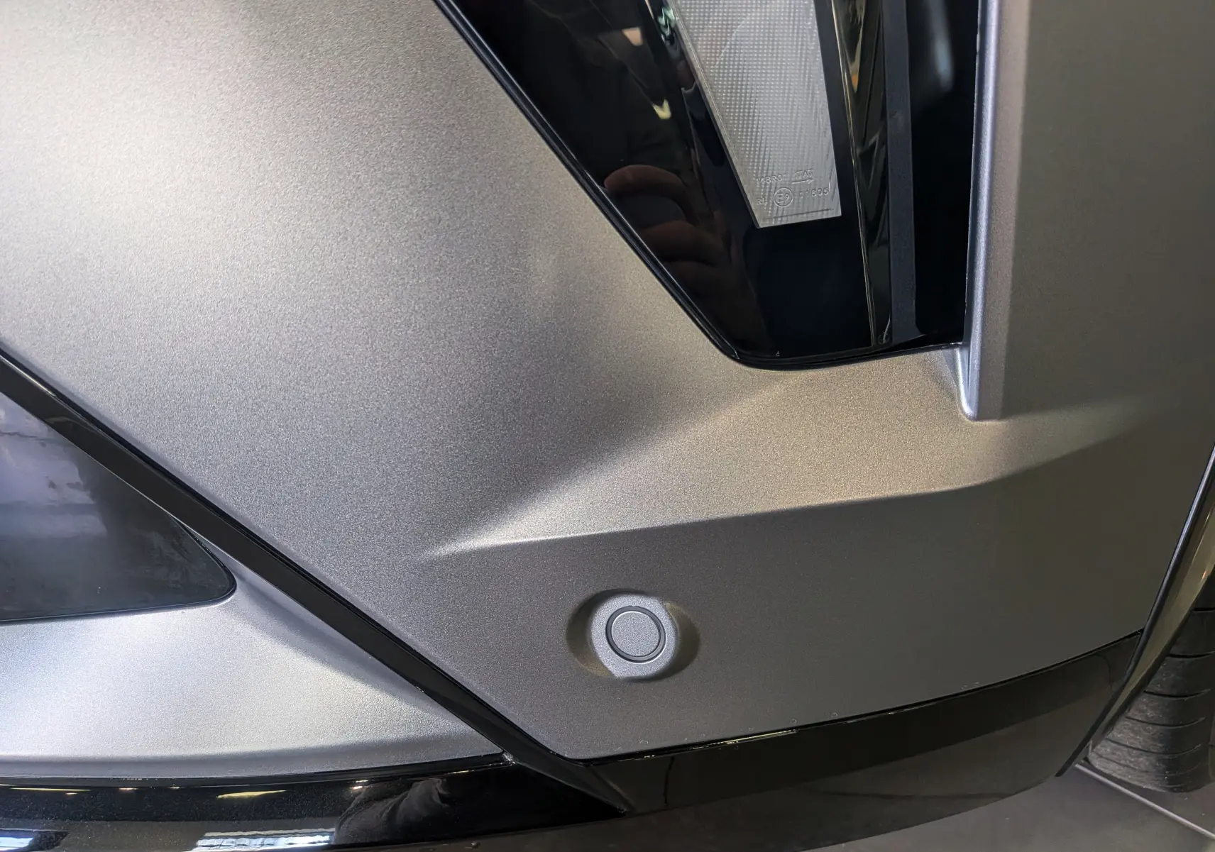 Gros plan sur le pare-chocs avant gris schiste satin de la Renault Rafale E-TECH, mettant en valeur un capteur de stationnement rond.