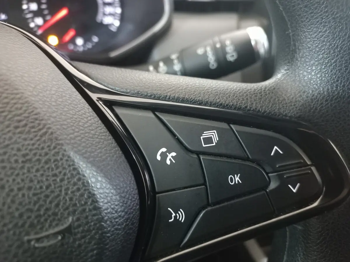 Gros plan sur les commandes noires du volant multifonctions d’une Renault Clio blanche, avec tableau de bord flou en arrière-plan.