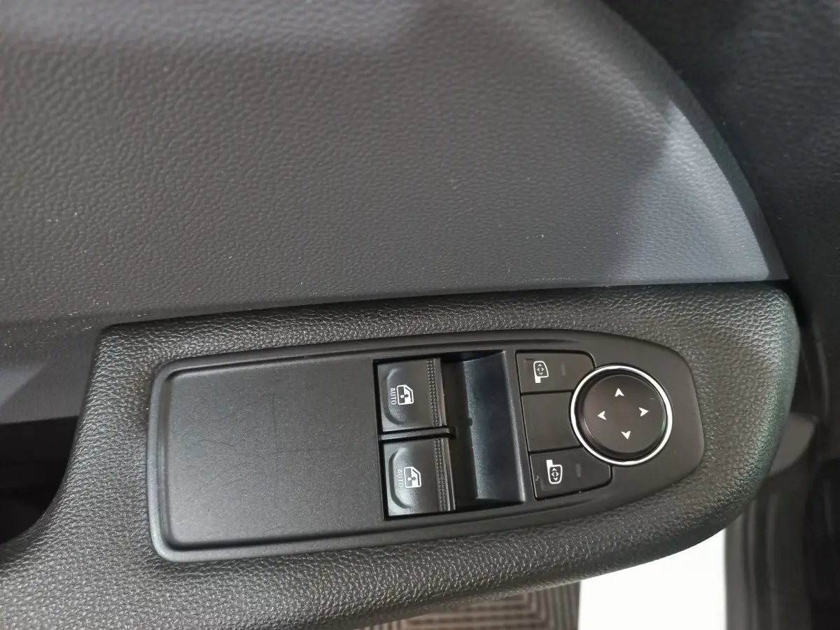 Gros plan sur les commandes de lève-vitres et réglage des rétroviseurs côté conducteur d'une Renault Clio blanche.