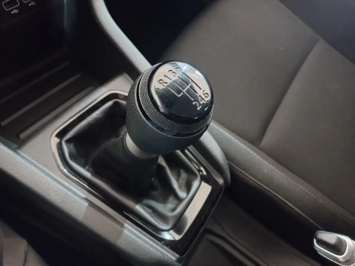 Gros plan sur le levier de vitesses manuel noir de la Renault Clio blanche, avec siège conducteur gris en arrière-plan.