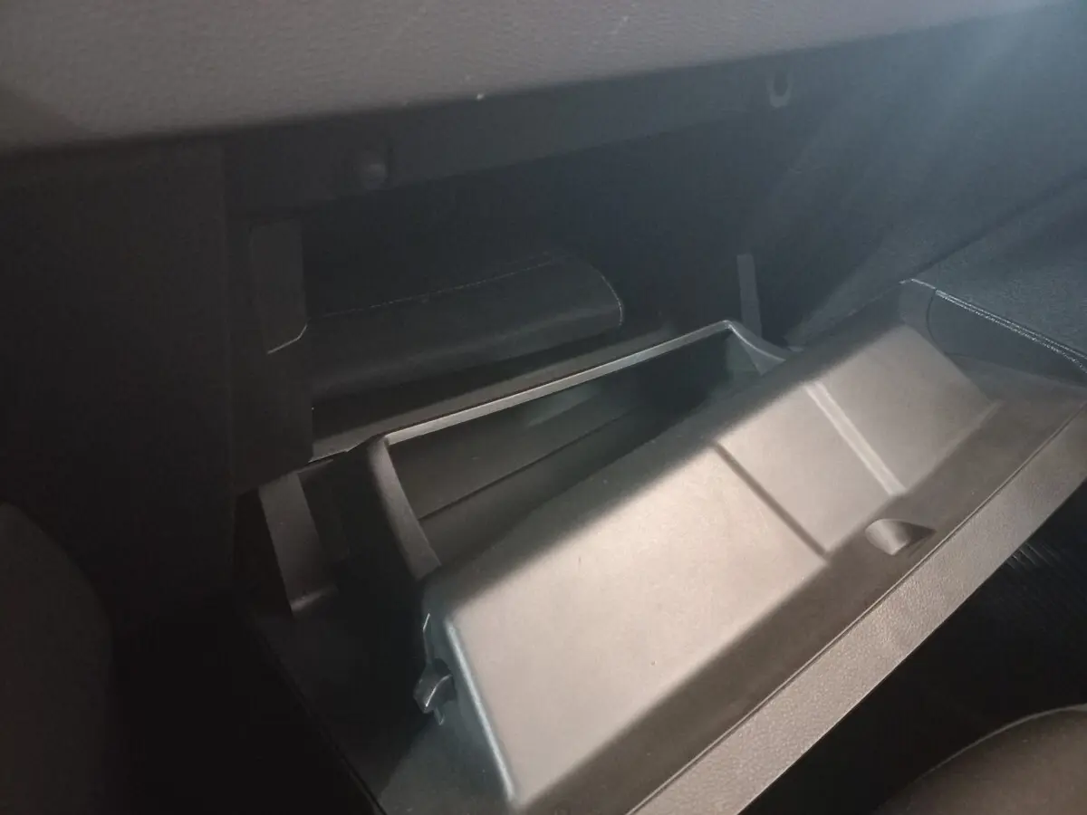 Vue rapprochée de la boîte à gants ouverte côté passager dans l’habitacle sombre d’une Renault Clio blanche.