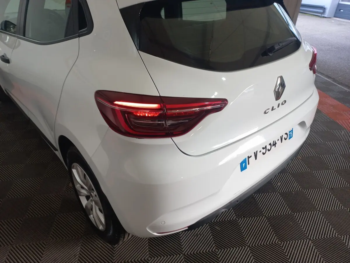 Vue 3/4 arrière droite d'une Renault Clio blanche de 2020 avec feux arrière LED allumés et logo visible.