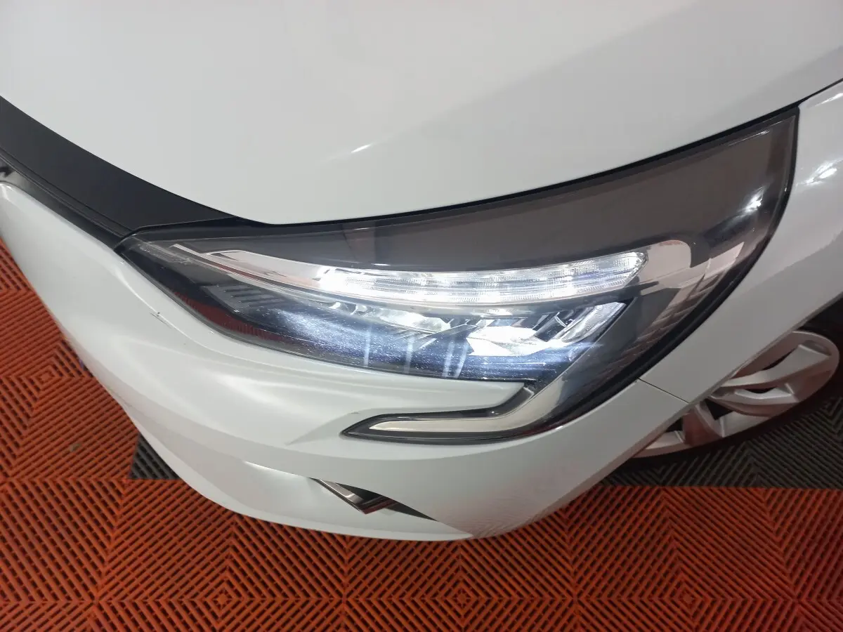 Gros plan sur le phare avant droit LED d’une Renault Clio blanche, avec partie du capot et pare-chocs visibles.