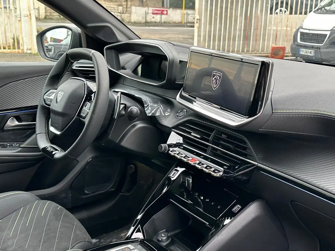 Vue intérieure côté conducteur du Peugeot 208 Hybrid 110 e-DCS6 GT 2025, avec volant compact, écran tactile et finitions noires.