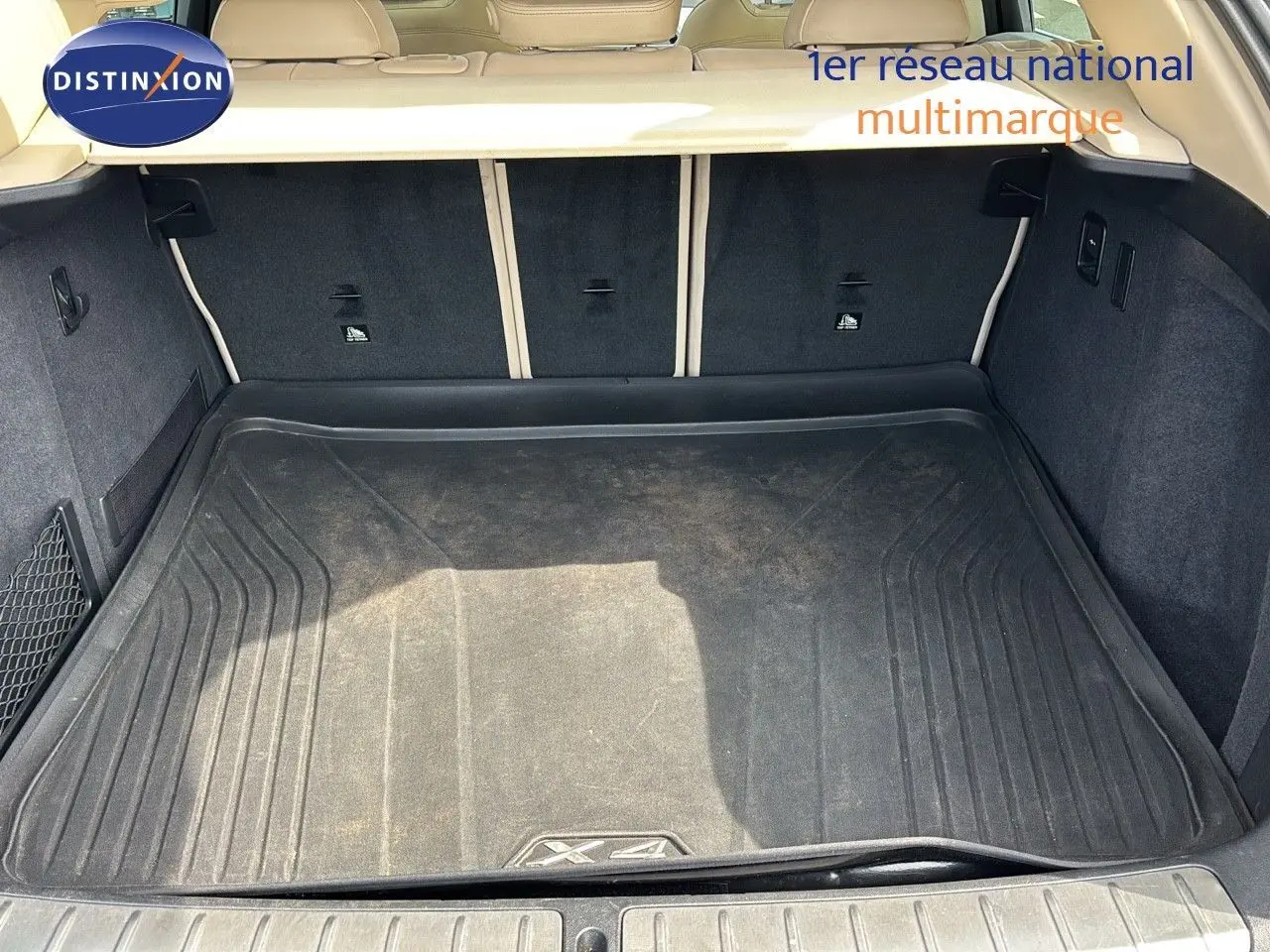 Coffre ouvert d'un BMW X4 XDRIVE 30D 2019, vue intérieure montrant le tapis de coffre noir et la garniture beige.