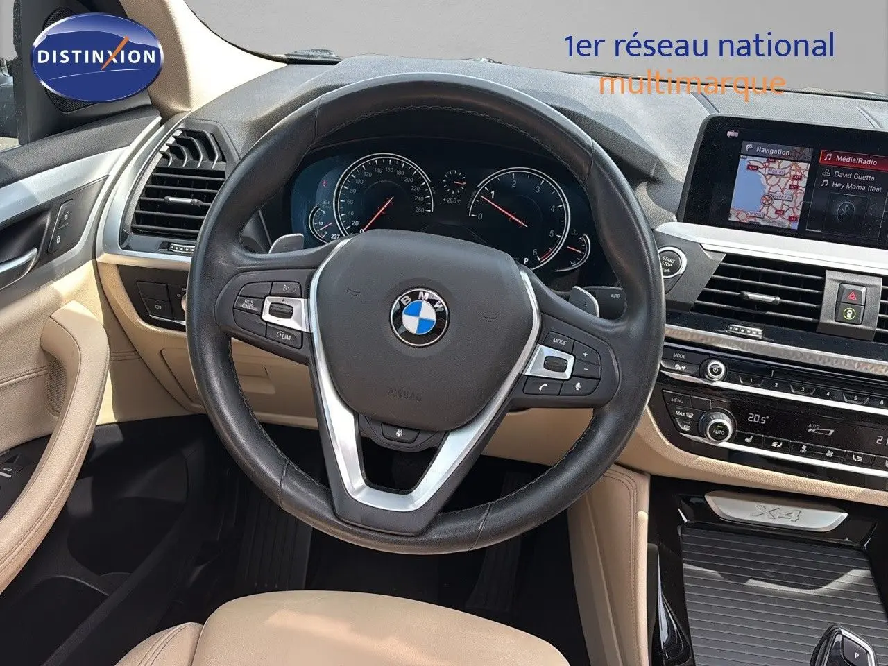 Vue intérieure du poste de conduite beige d'une BMW X4 30D 2019 avec volant cuir et écran multimédia intégré.