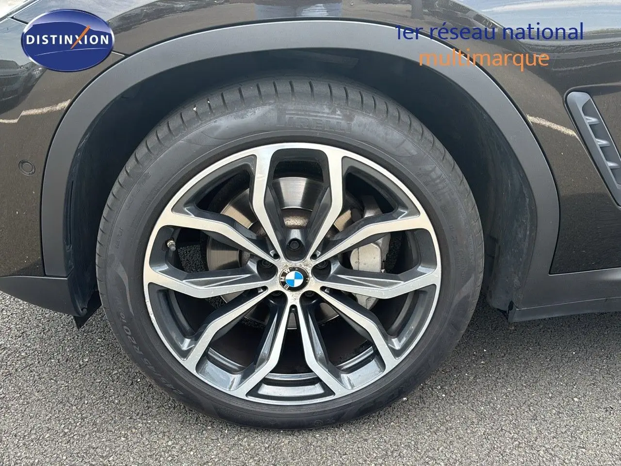 Gros plan sur la roue avant gauche d'un BMW X4 Sparkling Storm Métal avec jante alliage bicolore et logo BMW central.