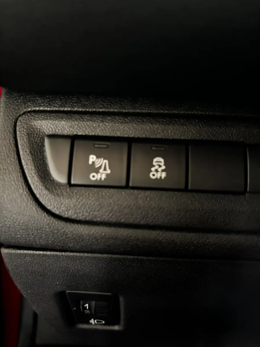 Gros plan sur les boutons de commande du système de stationnement et de l'antipatinage dans une Peugeot 208 rouge 1.6 THP 200 GTI.
