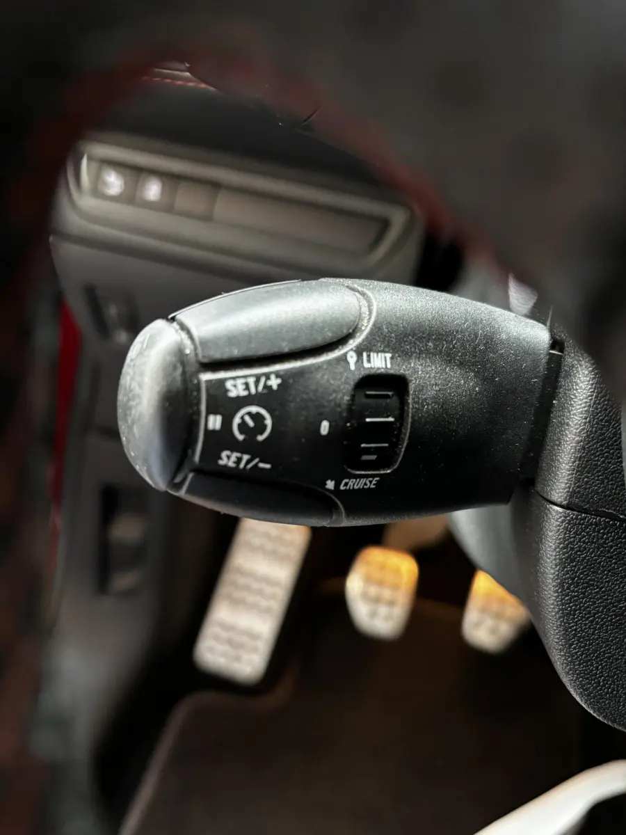 Gros plan sur la commande de régulateur de vitesse à gauche du volant d'une Peugeot 208 rouge essence de 2013.