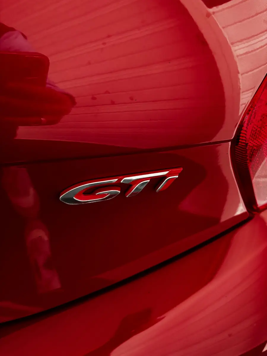 Gros plan sur l'emblème GTI à l'arrière droit d'une Peugeot 208 rouge brillante de 2013