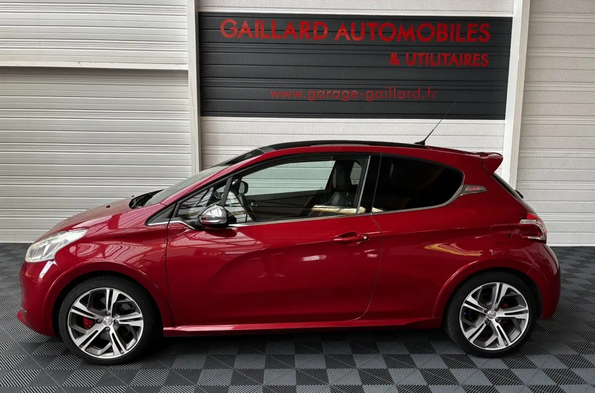 Profil côté gauche d'une Peugeot 208 GTI rouge avec jantes alliage et toit panoramique, en intérieur showroom.