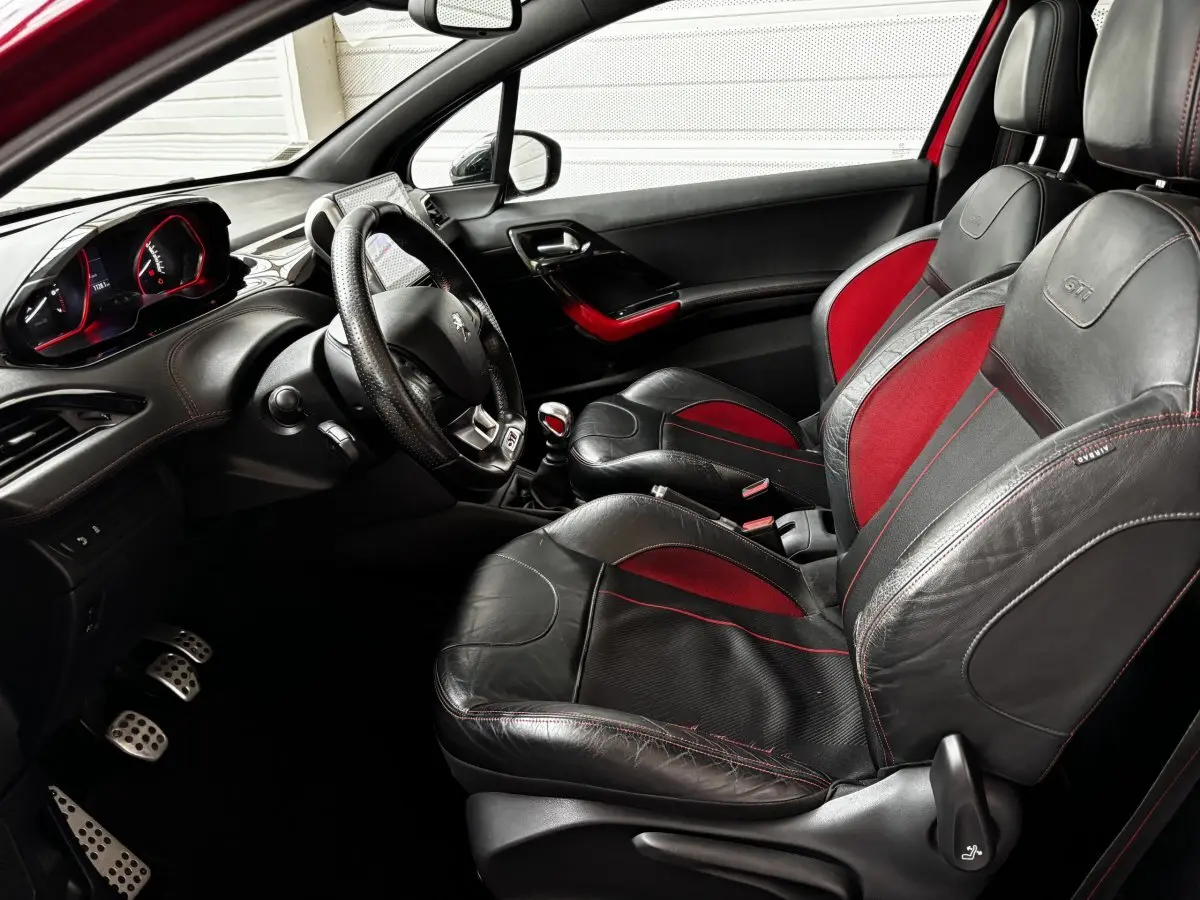 Intérieur avant droit de la Peugeot 208 GTI 2013, sièges cuir noir et rouge avec volant multifonctions et levier manuel.