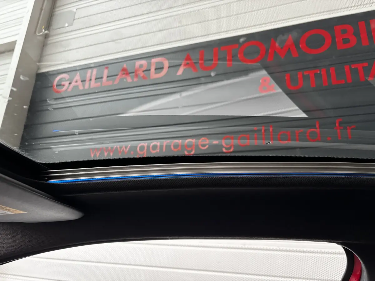 Vue intérieure du toit panoramique de la Peugeot 208 GTI rouge, mettant en valeur la vitre ouverte et le ciel visible.