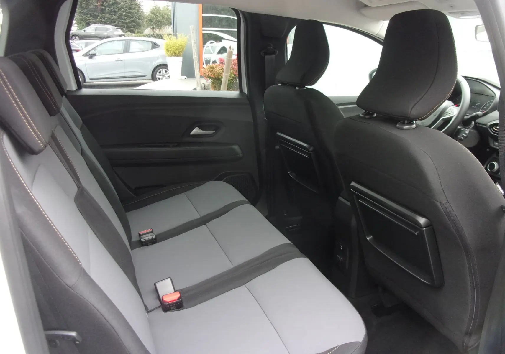Vue intérieure côté gauche du Dacia Jogger blanc 2025, montrant la banquette arrière grise et les dossiers avant noirs.