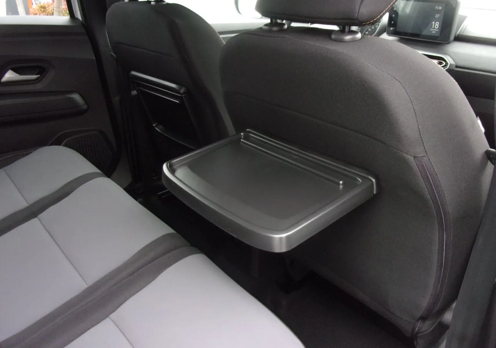 Vue intérieure arrière droite du Dacia Jogger 2025 avec tablette rabattable sur le dossier du siège avant et sièges gris.