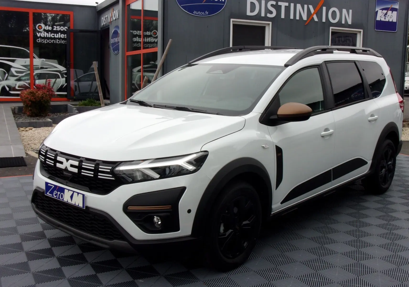 Vue 3/4 avant d'un Dacia Jogger blanc avec rétroviseurs marron et jantes noires, stationné devant un concessionnaire.