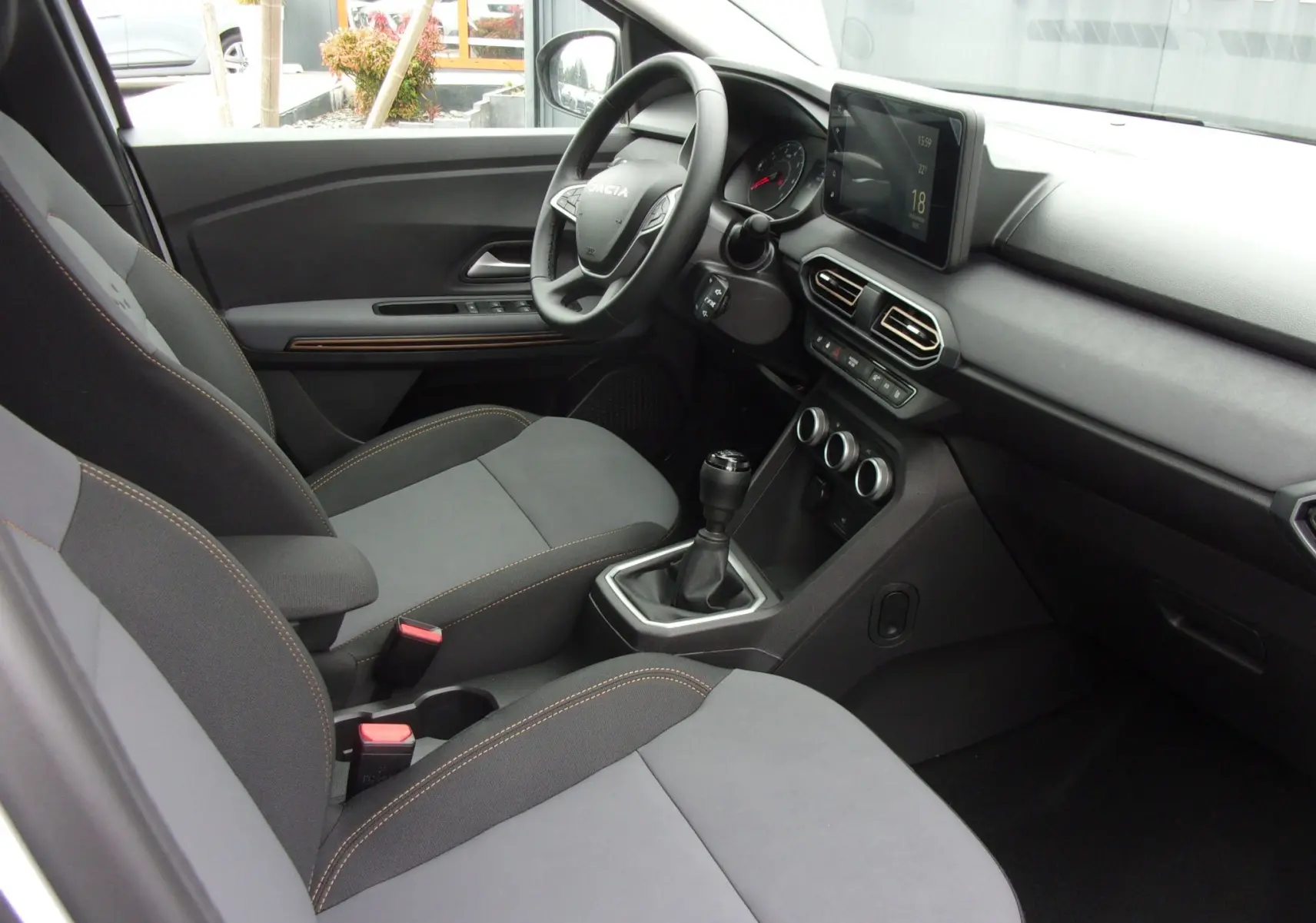 Vue intérieure côté conducteur du Dacia Jogger blanc 2025, montrant le tableau de bord moderne avec écran tactile et levier de vitesses manuel.