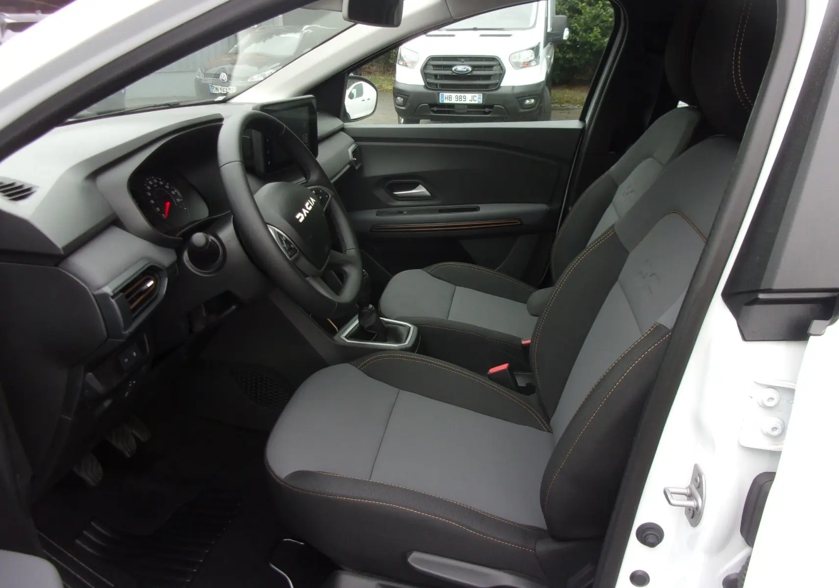 Vue intérieure côté conducteur du Dacia Jogger blanc 2025, mettant en valeur les sièges gris et la planche de bord moderne.